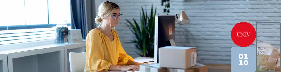 Person working at a computer in a modern office with boxes on the desk and a plant in the background