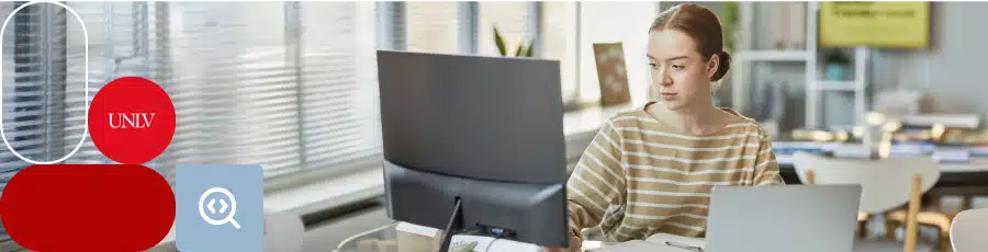 Person working at a desk with computer and laptop in an office, UNLV logo on the left.